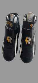 A pair of black high-top racing shoes with white side stripes and a gold 'R' logo on the sides, resting on a light gray textured fabric surface.