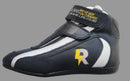 A black and white racing shoe with a yellow and white 'R' logo and a hook-and-loop strap closure, photographed on a gray textured fabric surface.